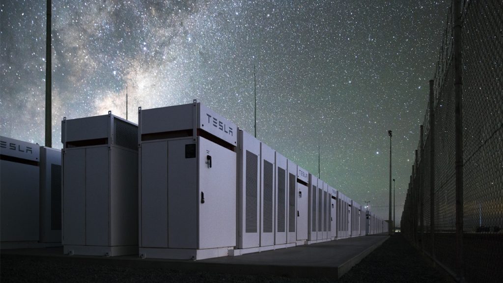 A Tesla battery bank outdoors under a starlit night sky.